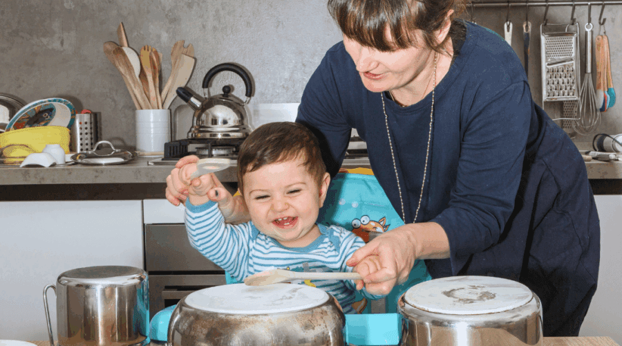 Smiling baby exploring early child development by playing with pots and pans, using a wooden spoon to make sounds